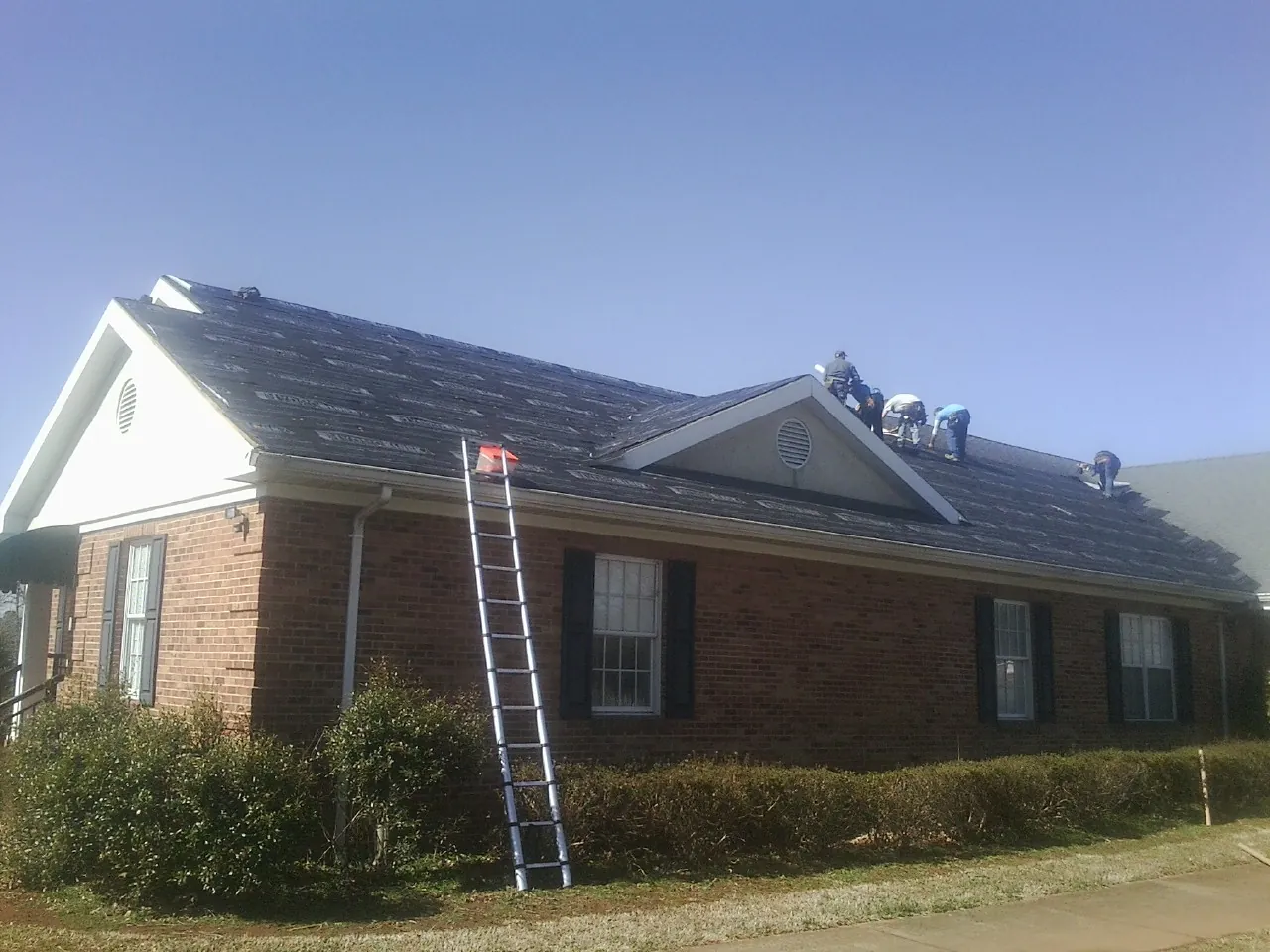 Crew tearing shingles off a brick ranch roof with a ladder set — Emergency Roof Repair work by our crew in Fall River