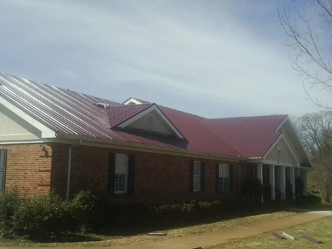 Red metal roof with gabled entries on a long brick building, from a Hail Damage Roof Repair job in Fall River