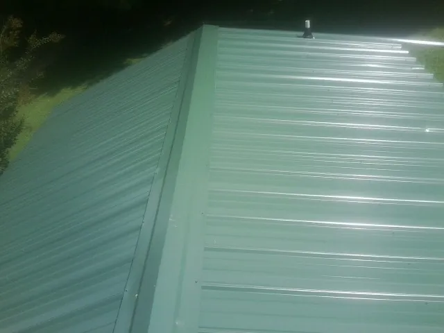 New green metal panels meeting at the ridge of a roof — Flat Roof Repair work by our crew in Fall River