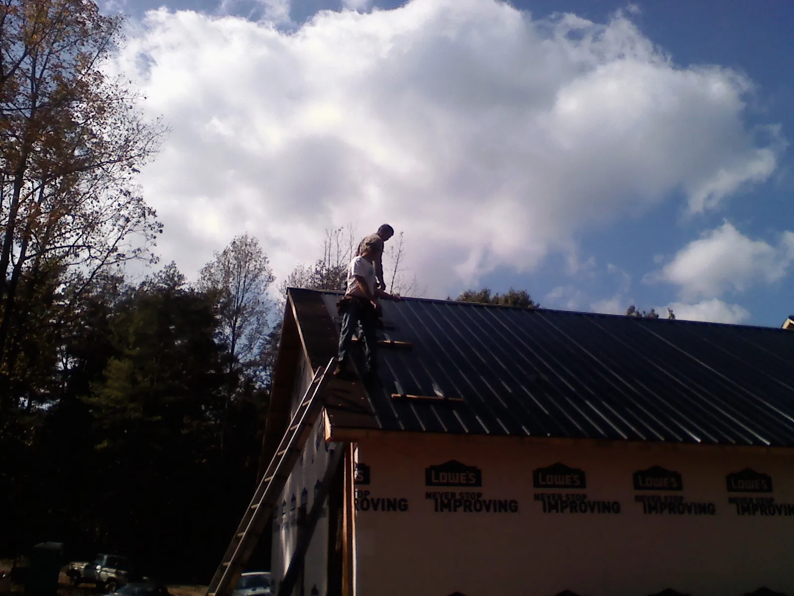 Roofer fastening dark metal panels high against a cloudy sky, from a Roof Inspection job in Fall River